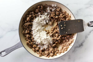 Adding flour to cooked breakfast sausage in a skillet.