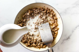 Adding whole milk to a skillet with sausage to make southern gravy.