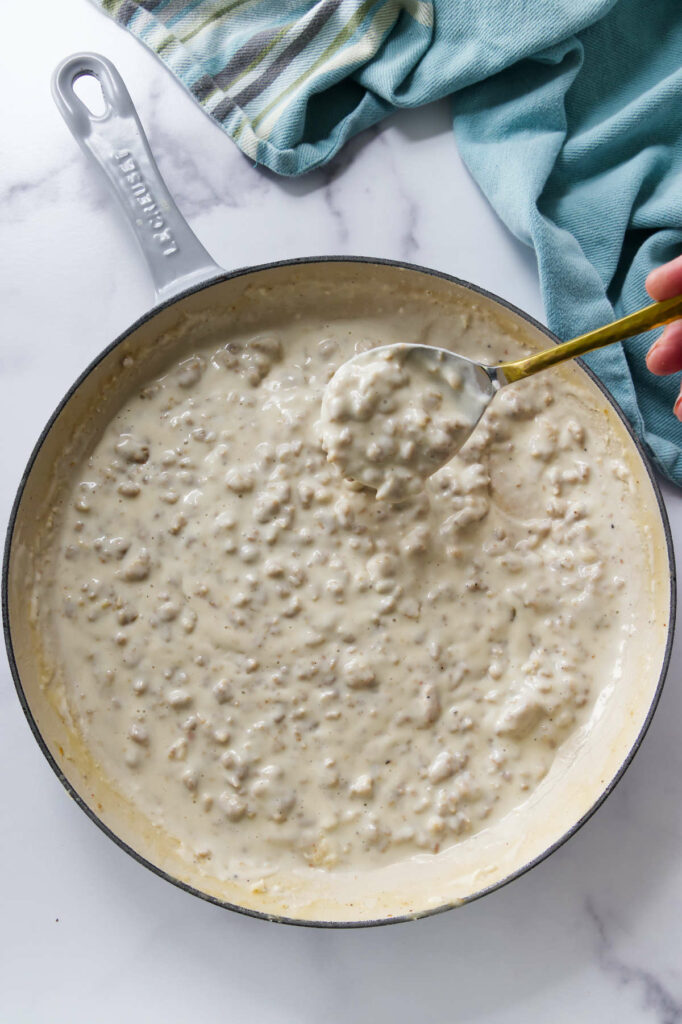 A spoon scooping homemade sausage gravy in a skillet.