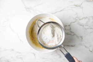 Sifting flour blend into a mixing bowl over batter.