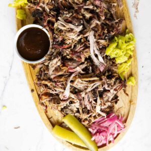 Shredded Boston pork butt on a cutting board with bbq sauce and pickled veggies.