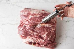 Hand injecting marinade into raw pork butt.