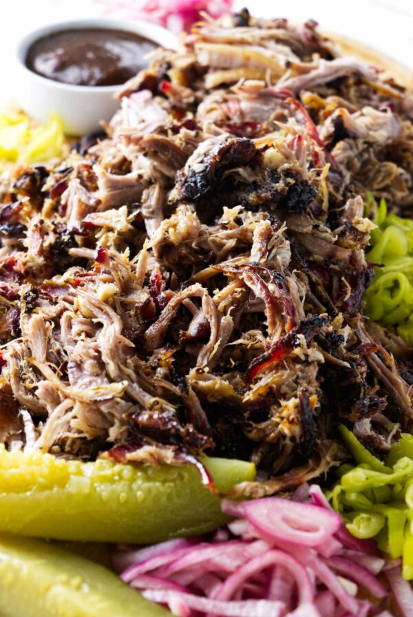 A pile of shredded pork butt with pickles and pickled red onions.