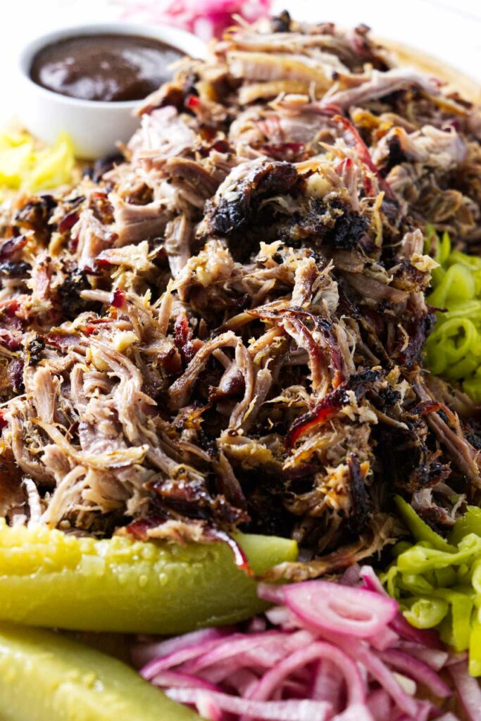 A pile of shredded pork butt with pickles and pickled red onions.