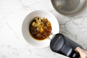 Beating sugar with brown butter in a mixing bowl.