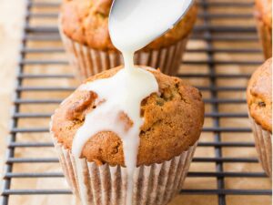 Drizzling orange glaze over zucchini muffins on a cooling rack.