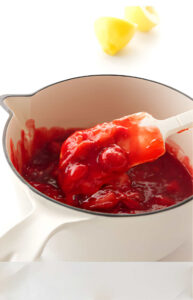 A spatula stirring strawberry sauce in a saucepan.