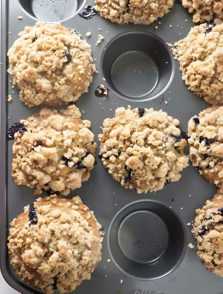 A muffin tin with hot muffins topped with streusel.
