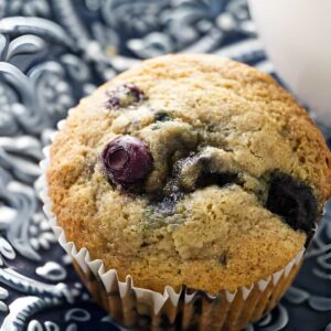 Spelt blueberry muffin in white liner on blue and white plate.