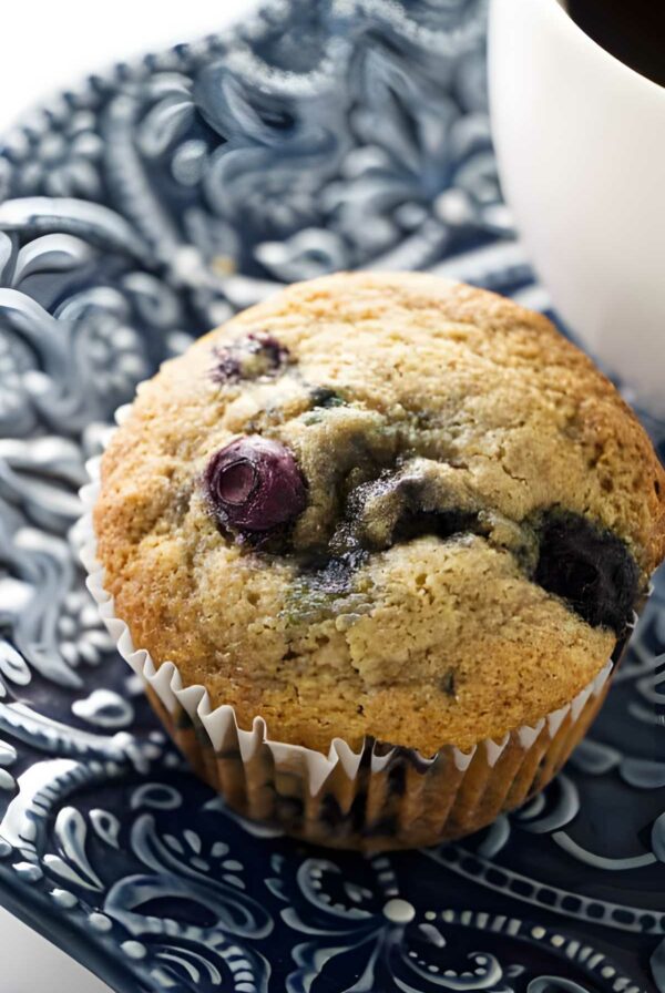 Spelt blueberry muffin in white liner on blue and white plate.