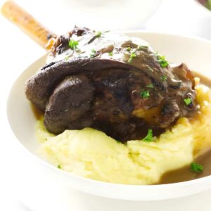 Lamb shank with gravy on mashed potatoes, garnished with parsley.