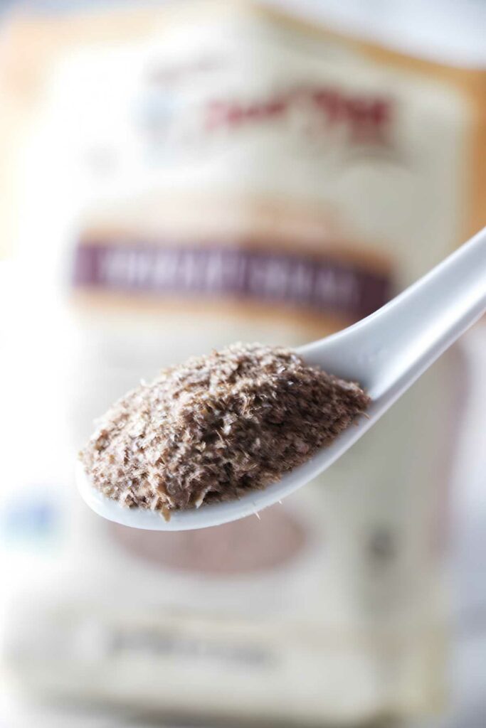 White spoon with dry bran, blurred package in background.