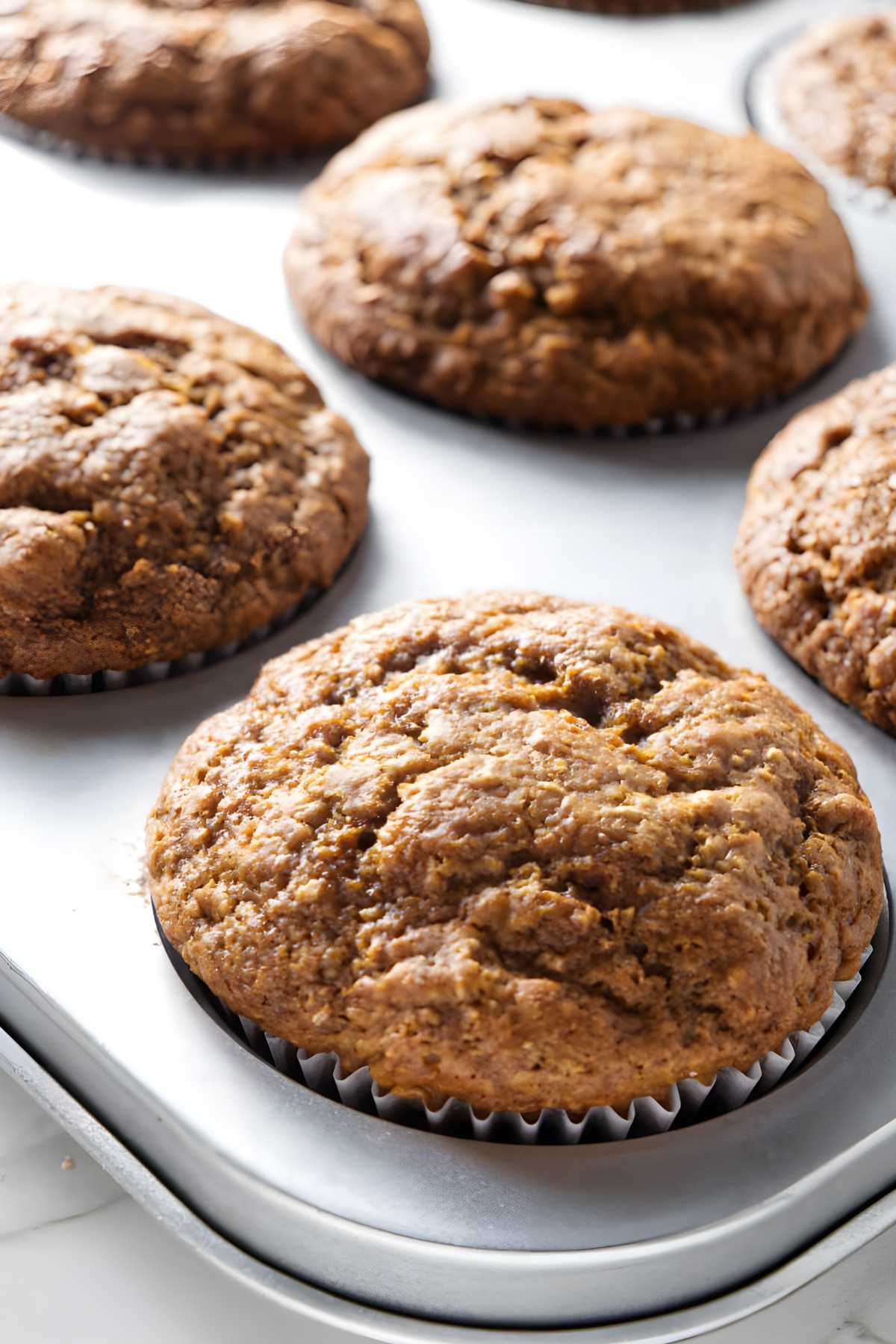 Freshly baked muffins in a metal tin, golden-brown tops and liners.