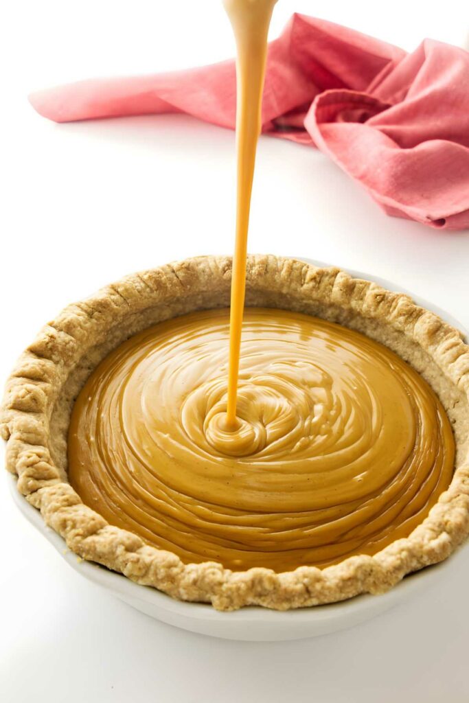 Buttersotch filling poured into baked pie crust, pink cloth in background.