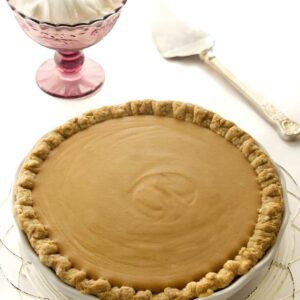 Golden-brown butterscotch pie on cake stand, vintage server and whipped cream behind.