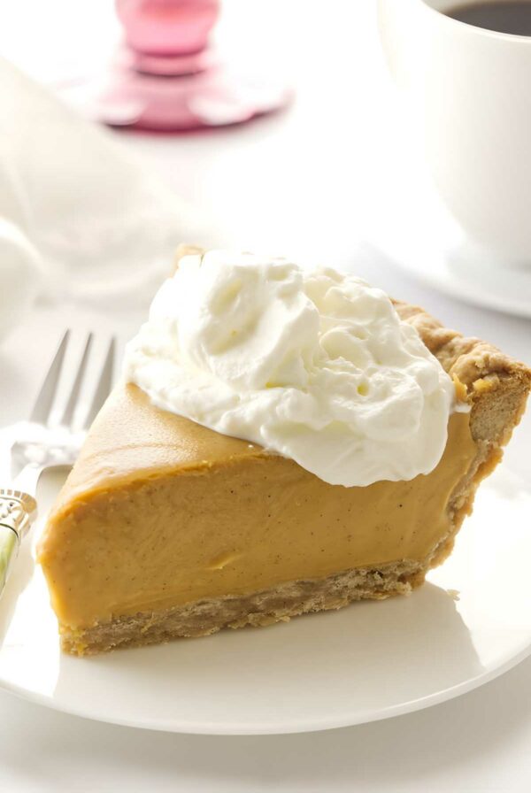 Butterscotch pie slice with whipped cream on white plate, fork nearby.