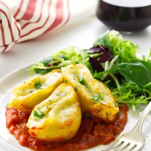 Stuffed pasta shells with tomato sauce and greens on a white plate.
