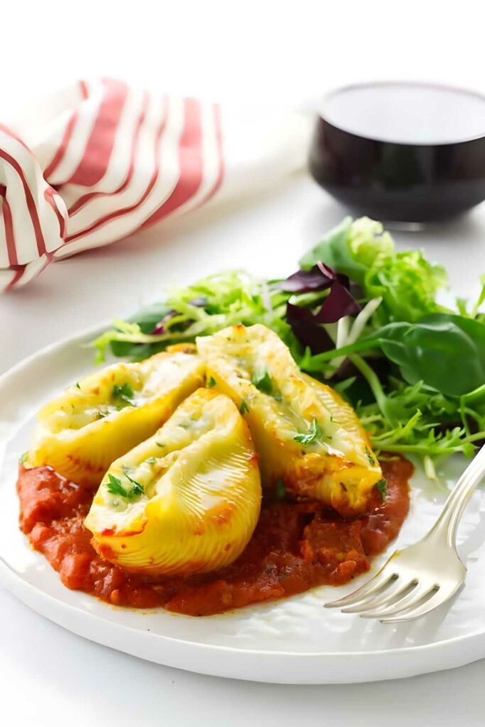 Stuffed pasta shells with tomato sauce and greens on a white plate.