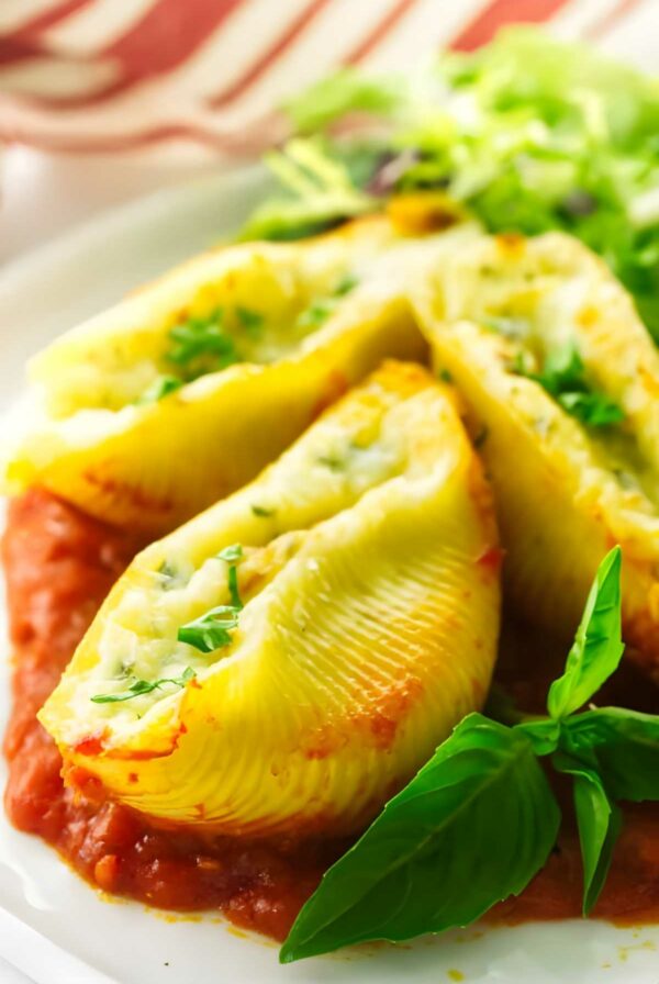 Stuffed pasta shells with ricotta on tomato sauce, garnished with basil.