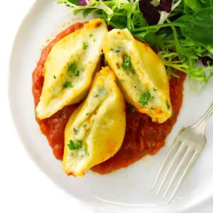 Three pasta shells stuffed with a cheese mixture on a plate with marinara sauce.