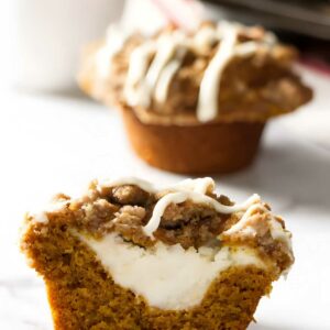 Pumpkin muffin halved, showing cheesecake filling, crumbly streusel, and white icing.