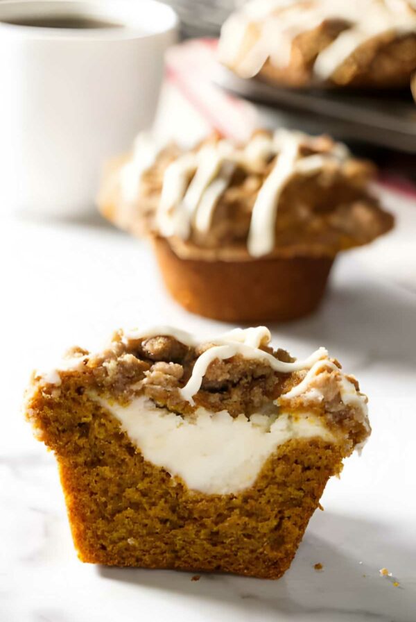 Pumpkin muffin halved, showing cheesecake filling, crumbly streusel, and white icing.
