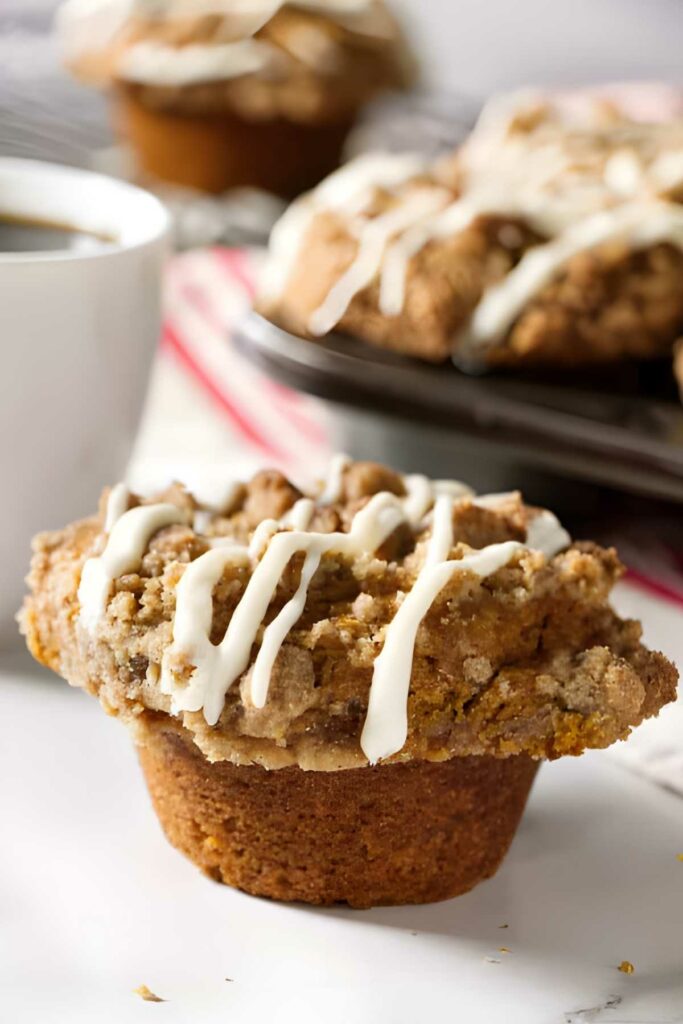 cheesecake stuffed pumpkin muffins Pumpkin muffins with white icing beside coffee; more muffins in background.