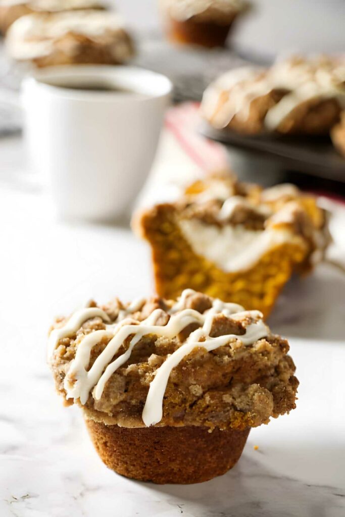 pumpkin muffins with cheesecake filling Pumpkin muffin with streusel and icing on marble, coffee and more muffins behind.