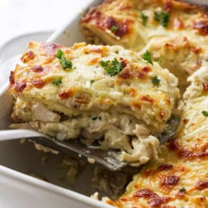 Cheesy chicken lasagna slice lifted from dish, showing layers and parsley.