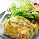 Cheesy enchilada casserole slice with salad on a plate.