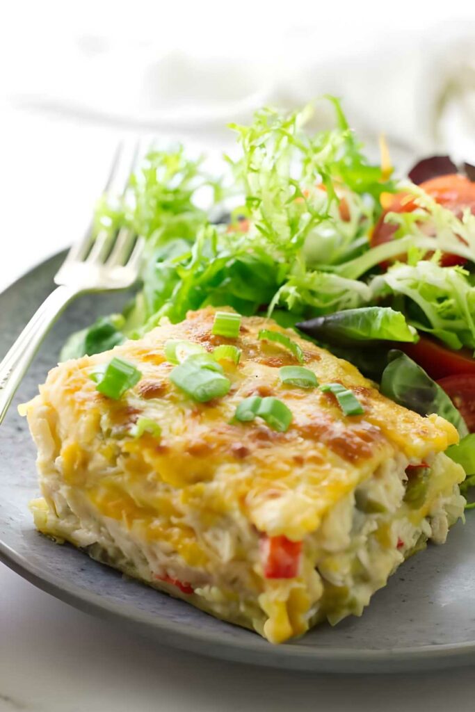 Cheesy enchilada casserole slice with salad on a plate.
