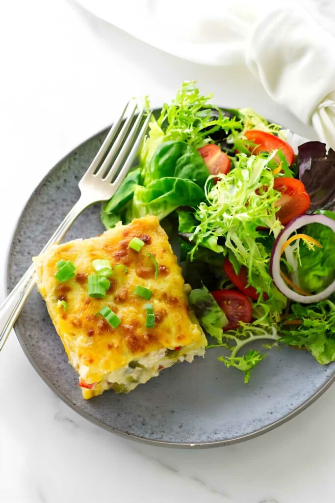 Cheesy enchilada casserole slice with green onions and salad on a plate.