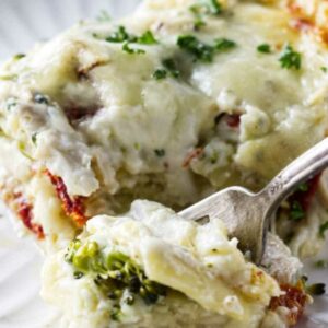Close-up of cheesy vegetable lasagna slice with a fork on a white plate.