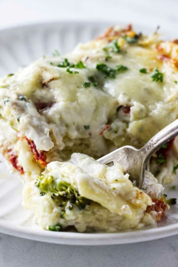 Close-up of cheesy vegetable lasagna slice with a fork on a white plate.