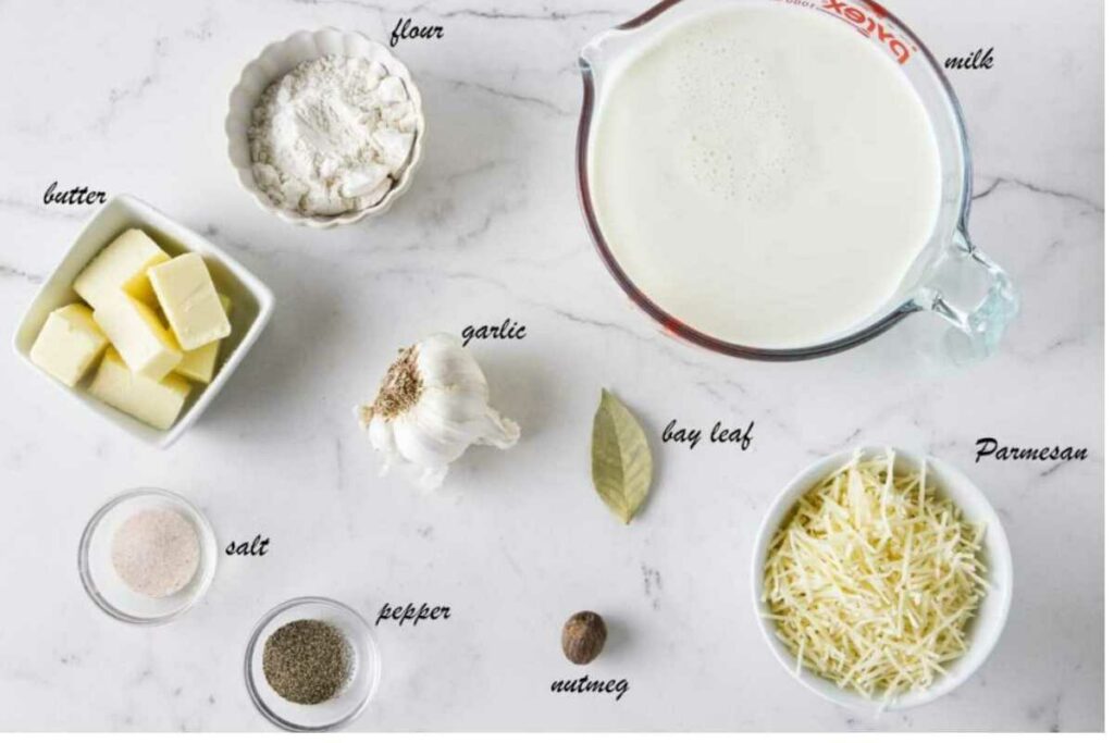 Baking ingredients on marble: flour, butter, Parmesan, milk, garlic, spices.