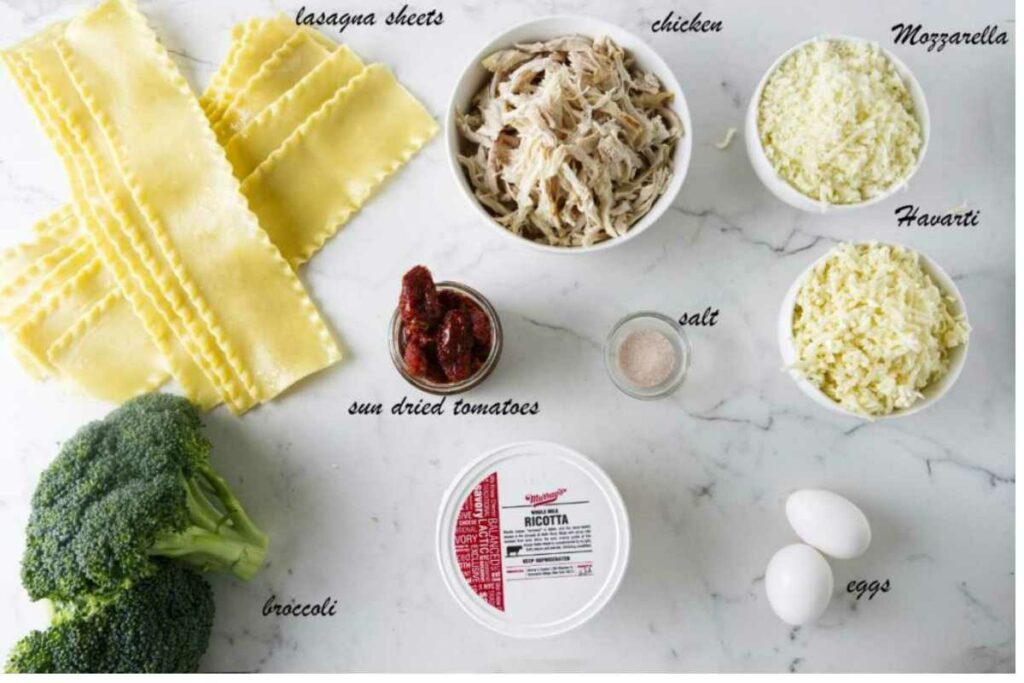 Lasagna ingredients arranged on a white surface, including cheeses, chicken, broccoli, and eggs.