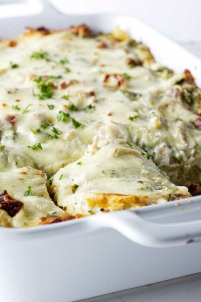 Cheesy baked lasagna in a white dish, one slice removed to show layers.
