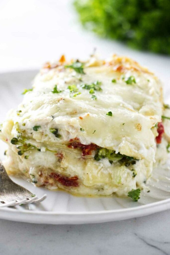 Slice of vegetable lasagna with visible layers and chopped parsley on white plate.