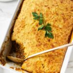 Golden brown casserole in white dish, topped with parsley, a serving scooped out.
