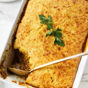 Golden brown casserole in white dish, topped with parsley, a serving scooped out.