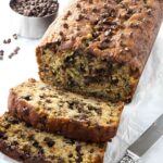 Chocolate chip banana bread with two slices cut, on parchment paper.