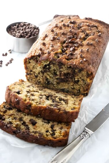 Chocolate chip banana bread with two slices cut, on parchment paper.