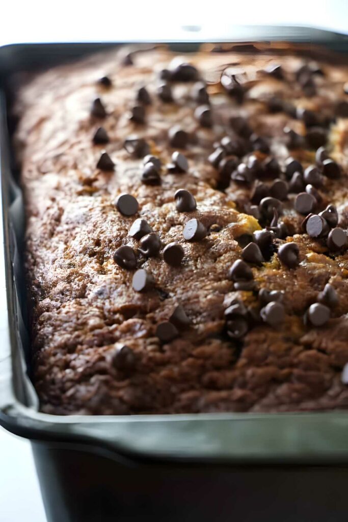 Close-up of banana bread with chocolate chips in a metal pan, golden brown.