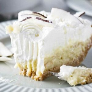Creamy coconut cream pie slice with whipped cream and coconut flakes, forkful missing.