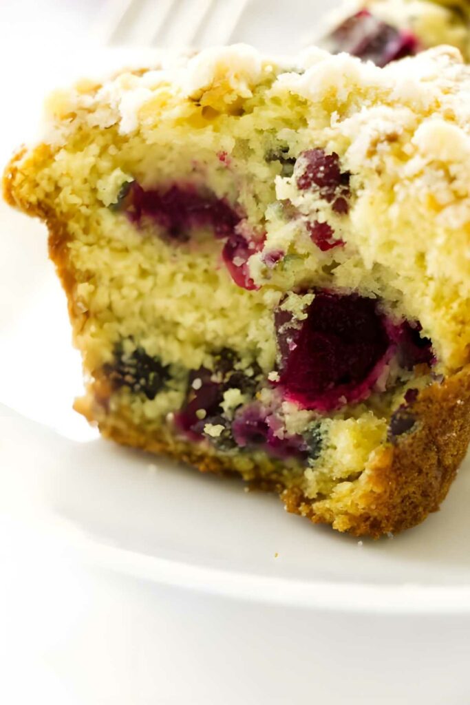 Close-up of a cranberry muffin with crumb topping on a white plate.