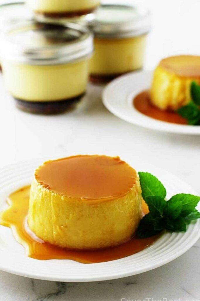Close-up of creamy flan with caramel sauce and mint on a white plate.