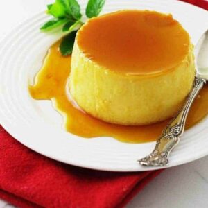 Flan with caramel sauce and mint on a white plate with spoon.