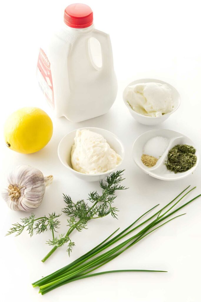 Ranch dressing ingredients arranged on white surface: milk, herbs, dairy, seasonings.