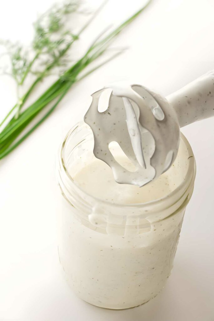 Jar of ranch dressing with blender, fresh dill and chives in background.