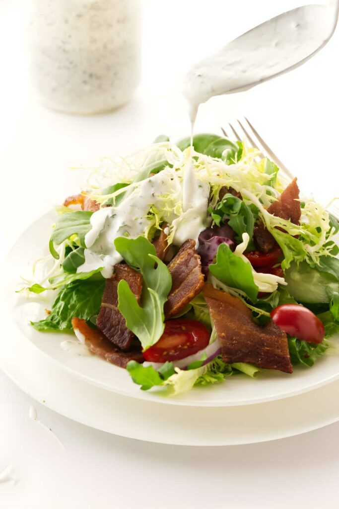 Fresh salad with bacon and ranch being drizzled from a spoon.